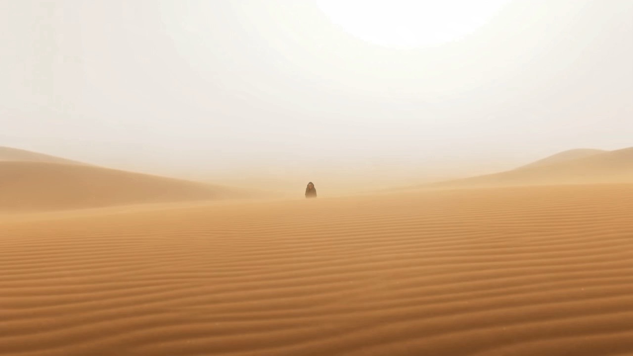 A lone figure crosses an endless dune under a white sun